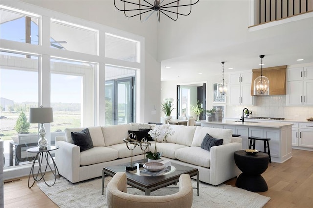 living area with a chandelier, light wood-type flooring, a high ceiling, and recessed lighting