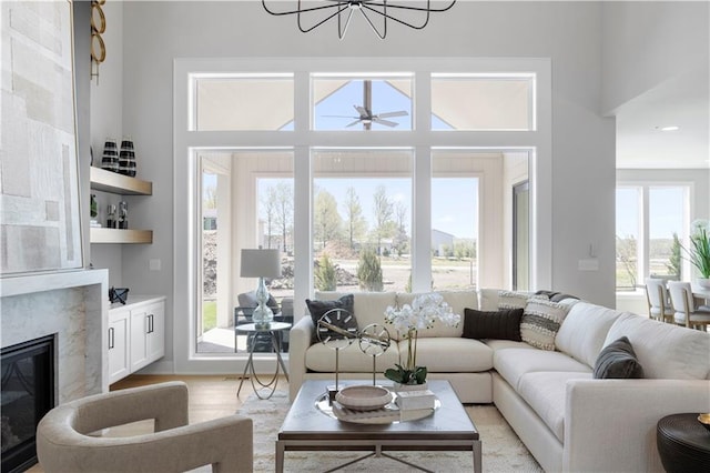 living area featuring a chandelier, a high end fireplace, light wood-style flooring, and a ceiling fan