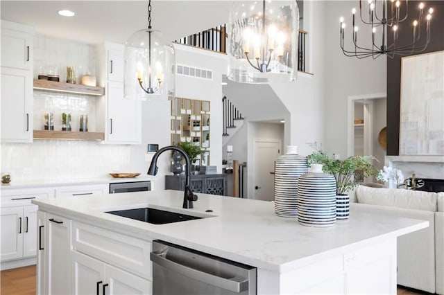 kitchen featuring a chandelier, stainless steel dishwasher, a sink, open shelves, and a center island with sink