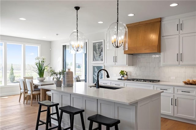 kitchen featuring a sink, a chandelier, stainless steel gas cooktop, tasteful backsplash, and a center island with sink