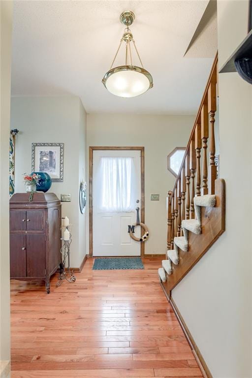 foyer entrance featuring light wood finished floors, baseboards, and stairway