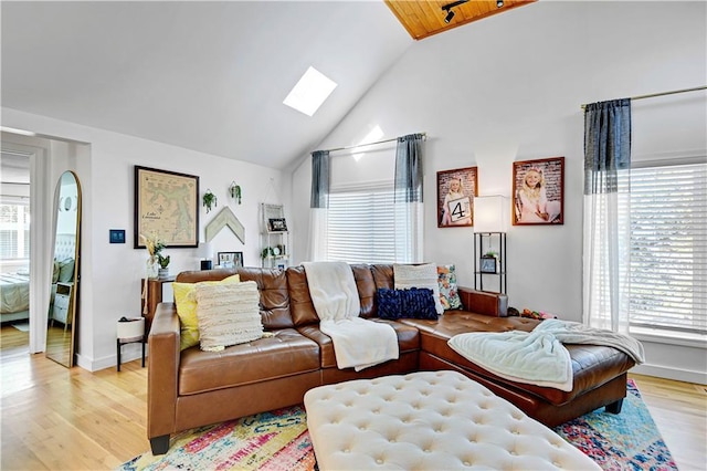 living room with light wood-type flooring, a skylight, plenty of natural light, and high vaulted ceiling