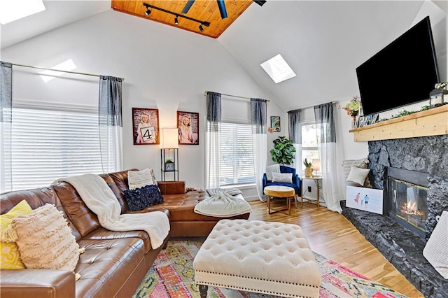 living room with a skylight, high vaulted ceiling, wood finished floors, and a stone fireplace