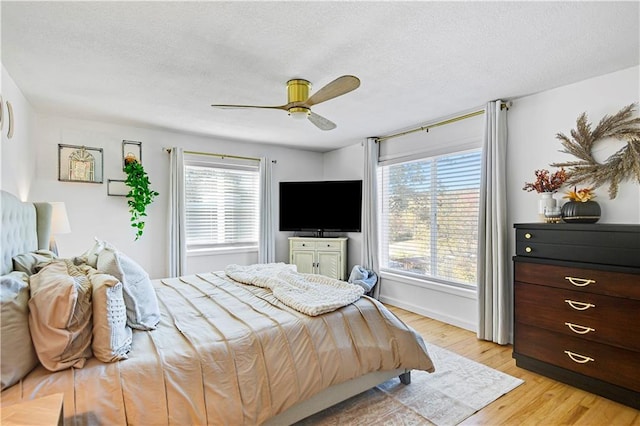 bedroom with a textured ceiling, ceiling fan, baseboards, and light wood-style floors