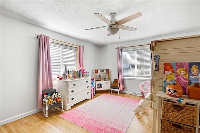 playroom with a textured ceiling, light wood finished floors, and baseboards