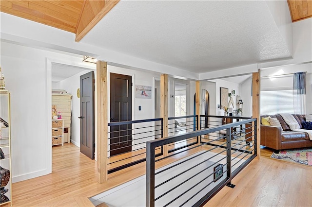 corridor with light wood-style floors, baseboards, a textured ceiling, and an upstairs landing