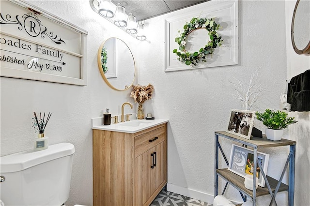 bathroom featuring a textured wall, toilet, vanity, baseboards, and tile patterned floors