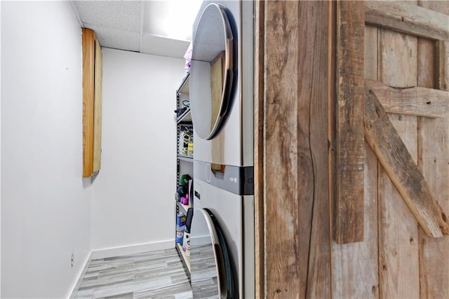 laundry room with stacked washer and dryer, baseboards, laundry area, and wood finished floors