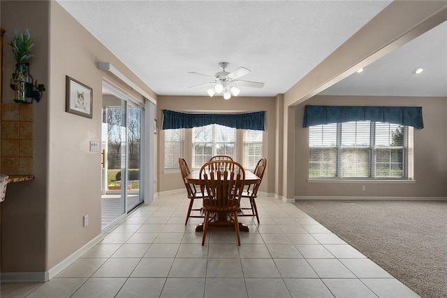 dining space featuring light carpet, a textured ceiling, baseboards, a ceiling fan, and light tile patterned floors