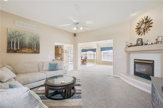 living room with a ceiling fan, light carpet, a tiled fireplace, baseboards, and visible vents
