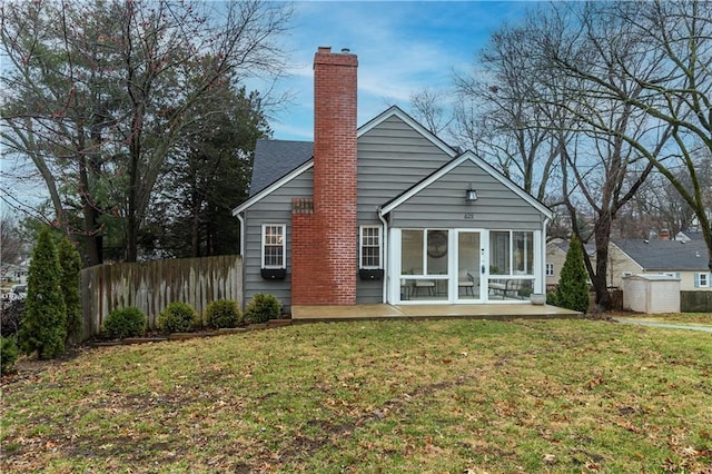 back of property featuring an outbuilding, fence, a sunroom, a lawn, and a chimney