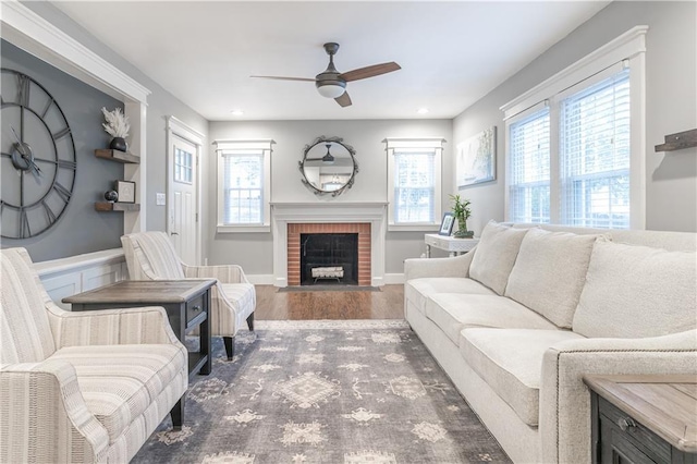 living room with a healthy amount of sunlight, a brick fireplace, a ceiling fan, and wood finished floors