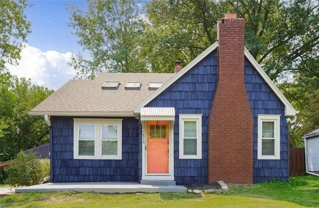 view of front of home featuring a front lawn, a chimney, and roof with shingles