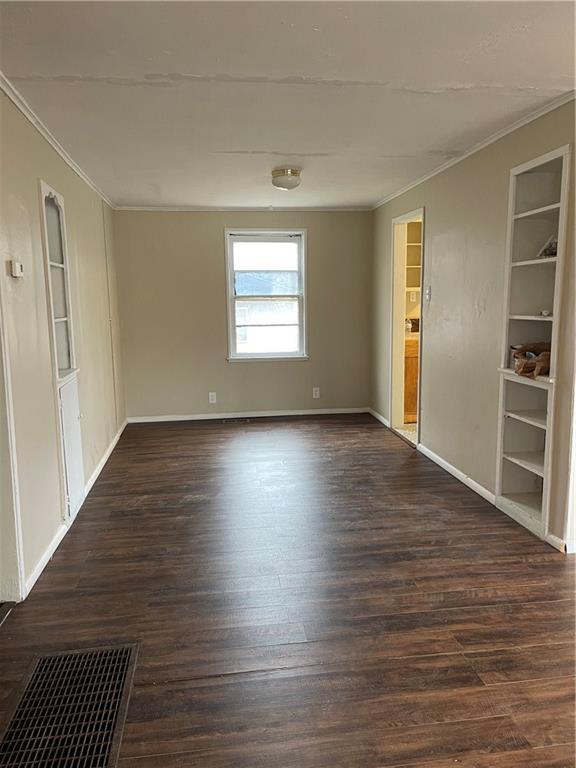 unfurnished room with baseboards, crown molding, visible vents, and dark wood-type flooring