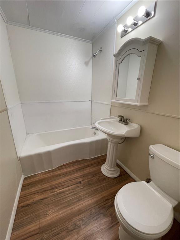 bathroom featuring baseboards, tub / shower combination, toilet, and wood finished floors