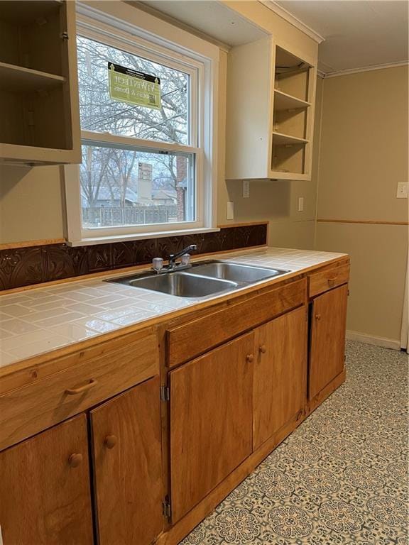 kitchen with tile counters, crown molding, light floors, open shelves, and a sink