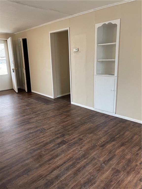 empty room featuring ornamental molding, dark wood-style flooring, and baseboards