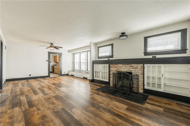 unfurnished living room featuring wood finished floors, baseboards, ceiling fan, a textured ceiling, and a brick fireplace