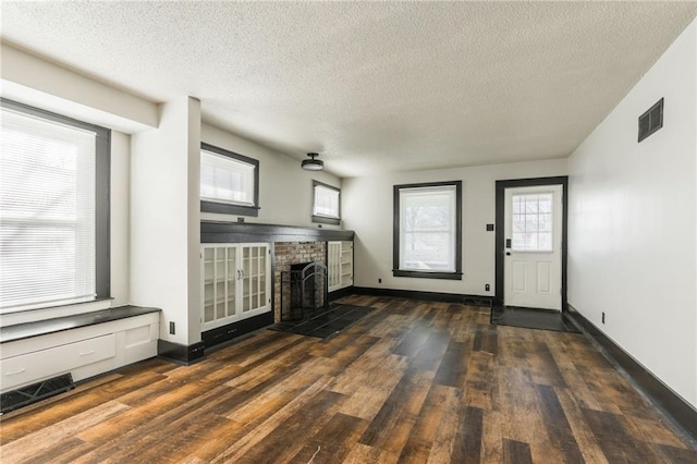 unfurnished living room featuring a brick fireplace, wood finished floors, visible vents, and baseboards