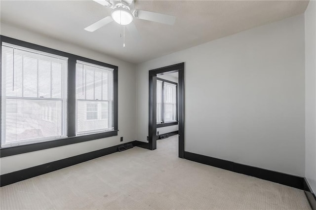 unfurnished room featuring a ceiling fan, visible vents, light colored carpet, and baseboards