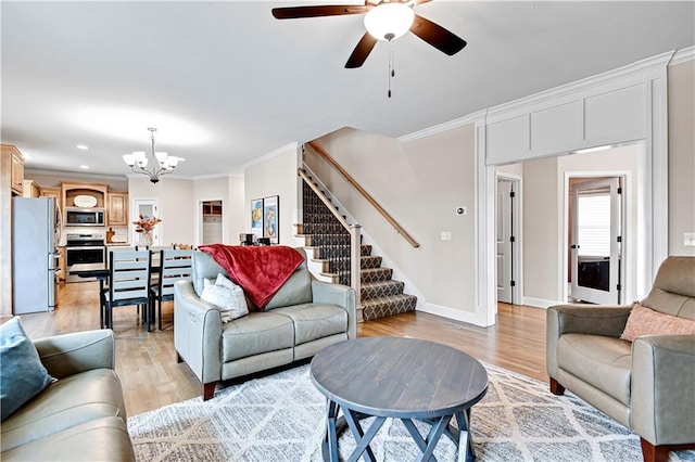 living area with stairs, light wood-style flooring, crown molding, and ceiling fan with notable chandelier