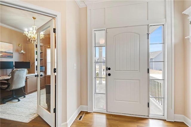 entrance foyer with a notable chandelier, crown molding, visible vents, and wood finished floors