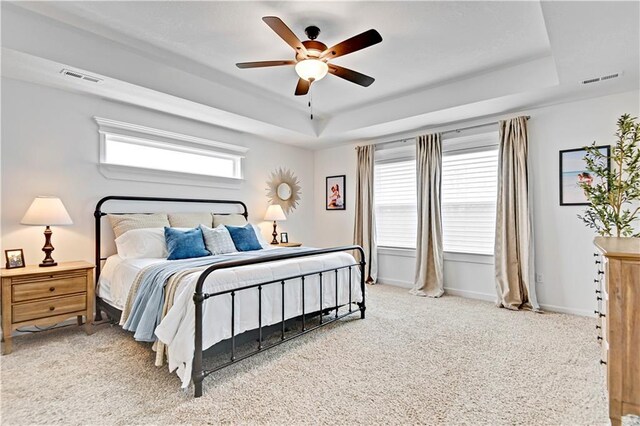 carpeted bedroom featuring visible vents, a raised ceiling, and baseboards