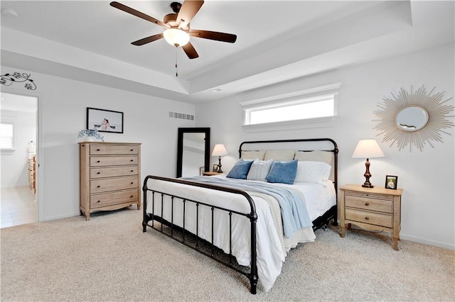 bedroom with a ceiling fan, baseboards, visible vents, a tray ceiling, and light carpet