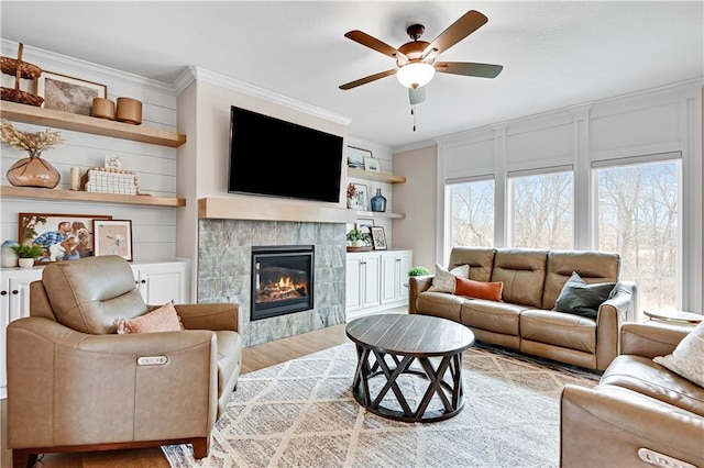 living area featuring a tile fireplace, wood finished floors, a ceiling fan, and ornamental molding