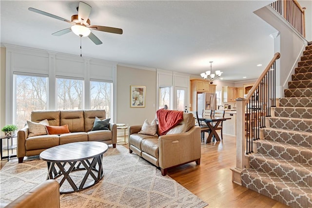 living room featuring recessed lighting, ornamental molding, stairs, light wood-style floors, and ceiling fan with notable chandelier