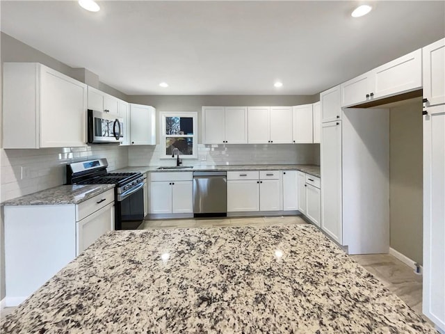 kitchen with light stone counters, decorative backsplash, appliances with stainless steel finishes, white cabinetry, and a sink