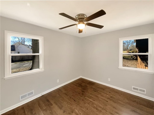 empty room with dark wood-style flooring, visible vents, ceiling fan, and baseboards