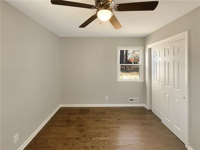 unfurnished bedroom featuring dark wood-style flooring, a closet, visible vents, and baseboards