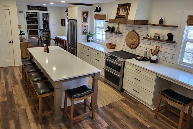 kitchen with a sink, light countertops, appliances with stainless steel finishes, a kitchen breakfast bar, and open shelves