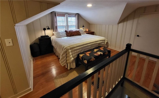 bedroom with vaulted ceiling, a decorative wall, and wood finished floors