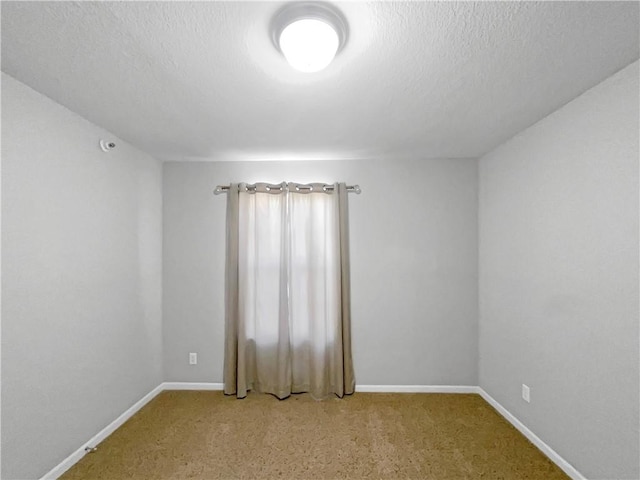 carpeted empty room featuring a textured ceiling and baseboards