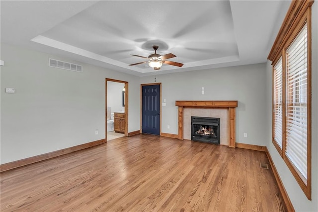 unfurnished living room featuring light wood-type flooring, a tray ceiling, and visible vents