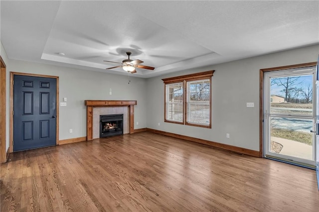 unfurnished living room featuring a healthy amount of sunlight, baseboards, a raised ceiling, and wood finished floors