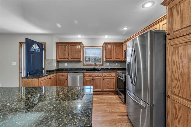 kitchen featuring light wood finished floors, stainless steel appliances, tasteful backsplash, a sink, and dark stone countertops