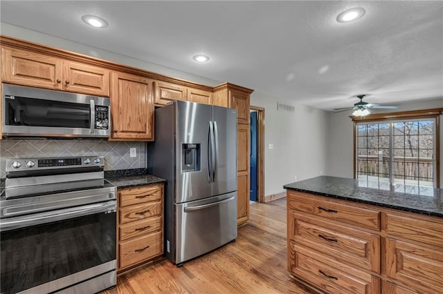 kitchen featuring visible vents, backsplash, light wood-style flooring, appliances with stainless steel finishes, and dark stone countertops