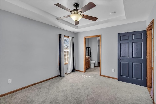 unfurnished bedroom with a tray ceiling, a ceiling fan, light carpet, connected bathroom, and baseboards