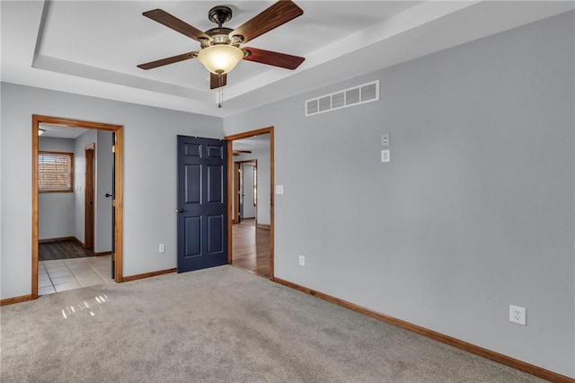 unfurnished bedroom with a tray ceiling, visible vents, a ceiling fan, carpet flooring, and baseboards