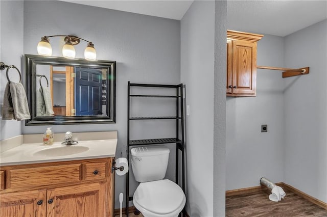 bathroom featuring toilet, baseboards, wood finished floors, and vanity