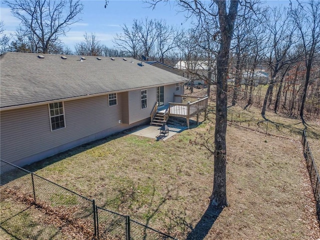 back of property with a yard, a shingled roof, a wooden deck, and fence