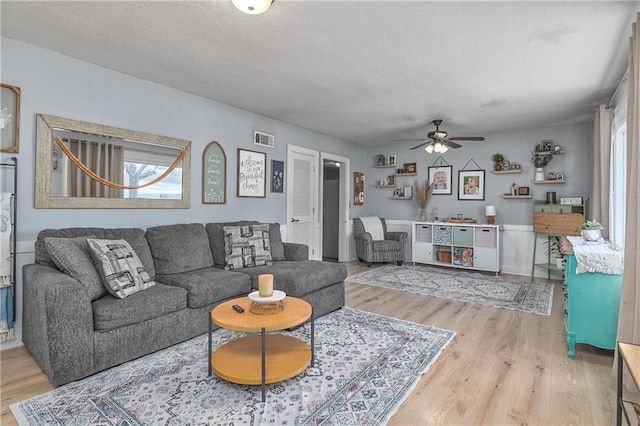 living room with a ceiling fan, light wood-style floors, visible vents, and a textured ceiling