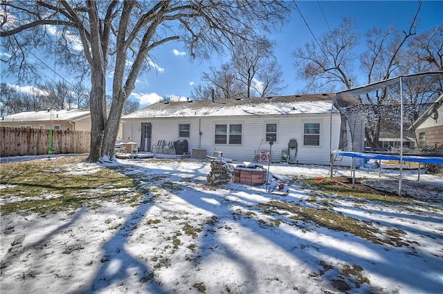 snow covered back of property with a trampoline and fence