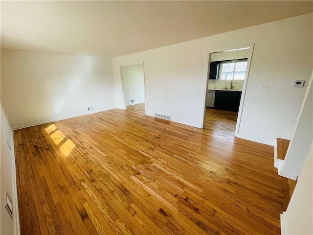 empty room with light wood-type flooring, visible vents, and a sink