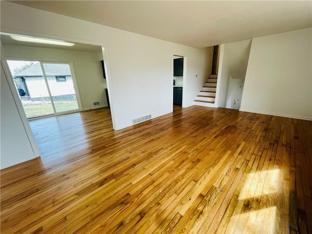 unfurnished room with visible vents, wood-type flooring, baseboards, and stairway