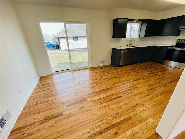 kitchen with a sink, stainless steel appliances, dark cabinets, and light wood-style flooring