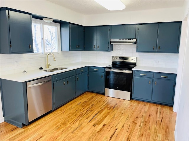 kitchen featuring under cabinet range hood, decorative backsplash, light wood-style flooring, appliances with stainless steel finishes, and a sink